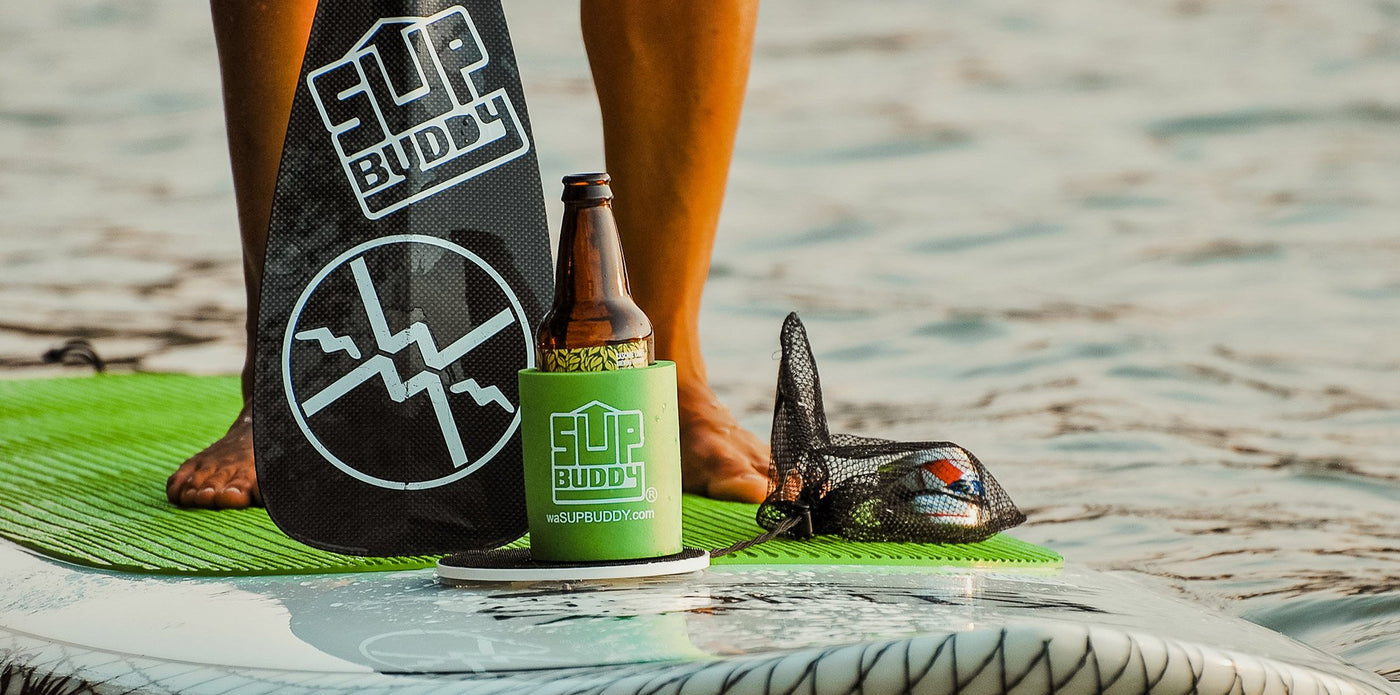 A zoomed in photo of a SUPBUDDY Koozie on a stand up paddleboard on the beach.